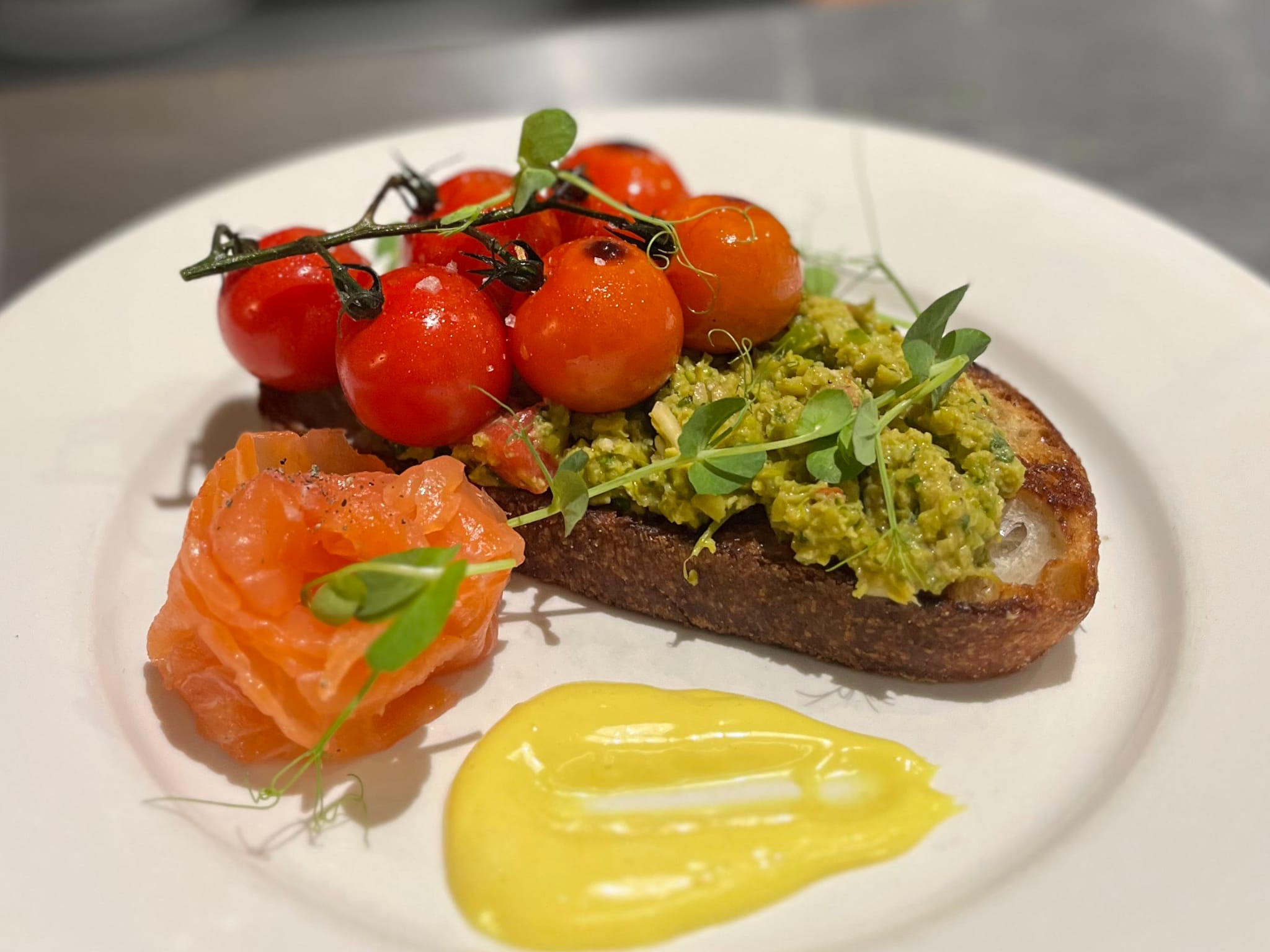 Smoked salmon, pea and broadbean guacamole, tomatoes on sourdough.